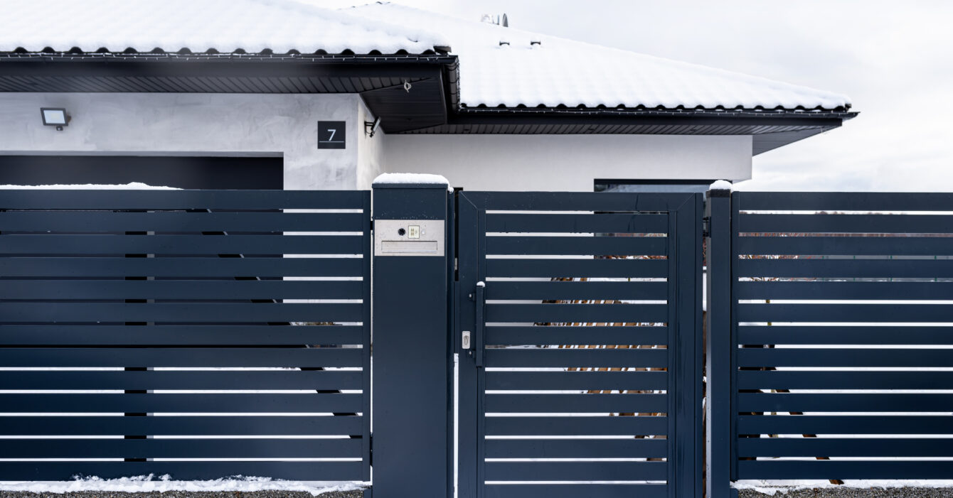 A modern gate with a letterbox and a wireless card reader, mounted in an anthracite panel fence, covered with snow.
