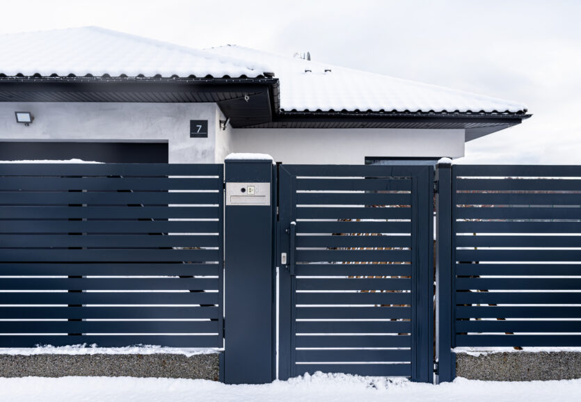 A modern gate with a letterbox and a wireless card reader, mounted in an anthracite panel fence, covered with snow.