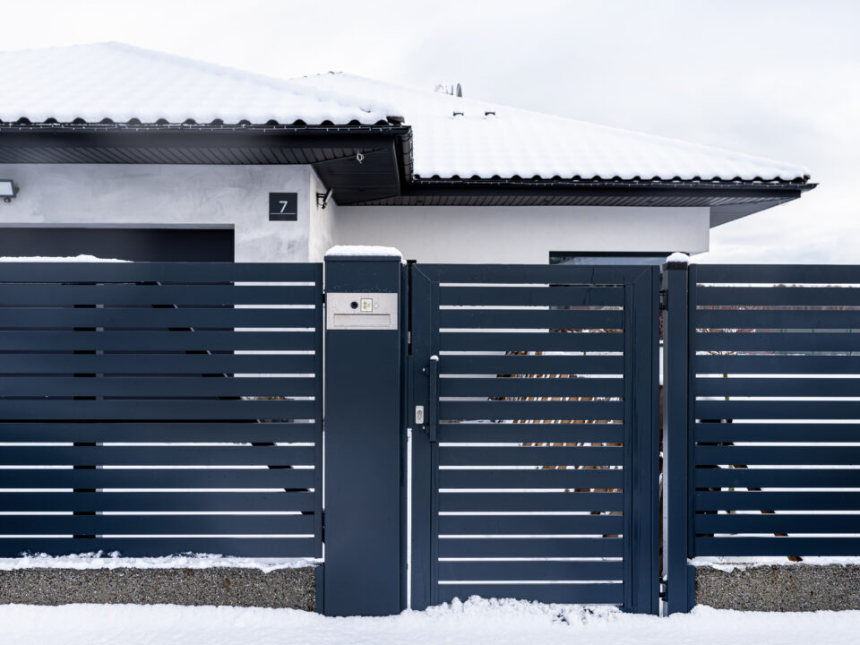 A modern gate with a letterbox and a wireless card reader, mounted in an anthracite panel fence, covered with snow.