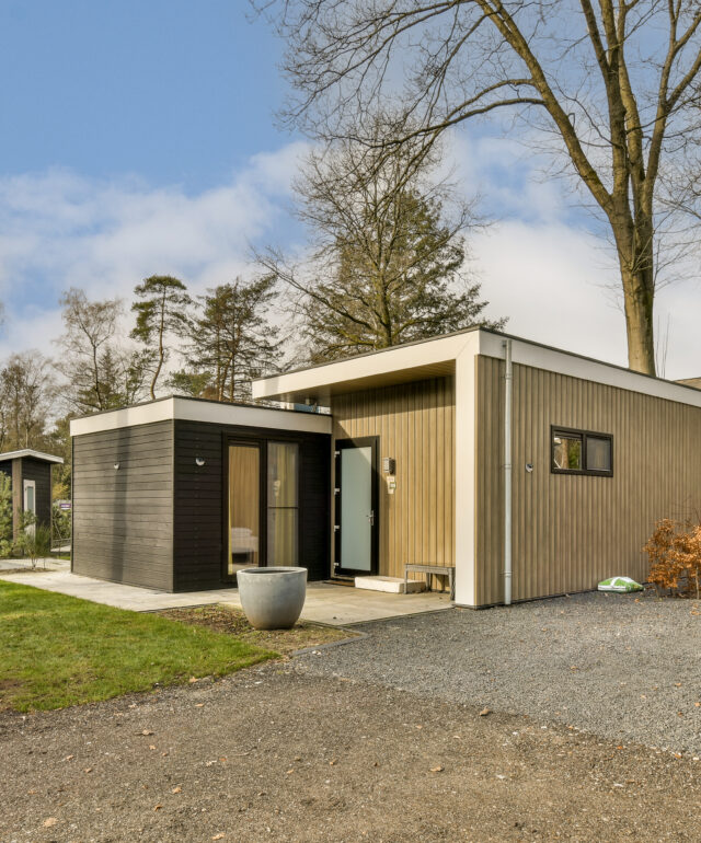 a small wooden house with a gravel driveway and trees