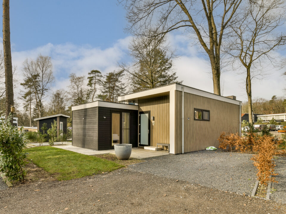 a small wooden house with a gravel driveway and trees